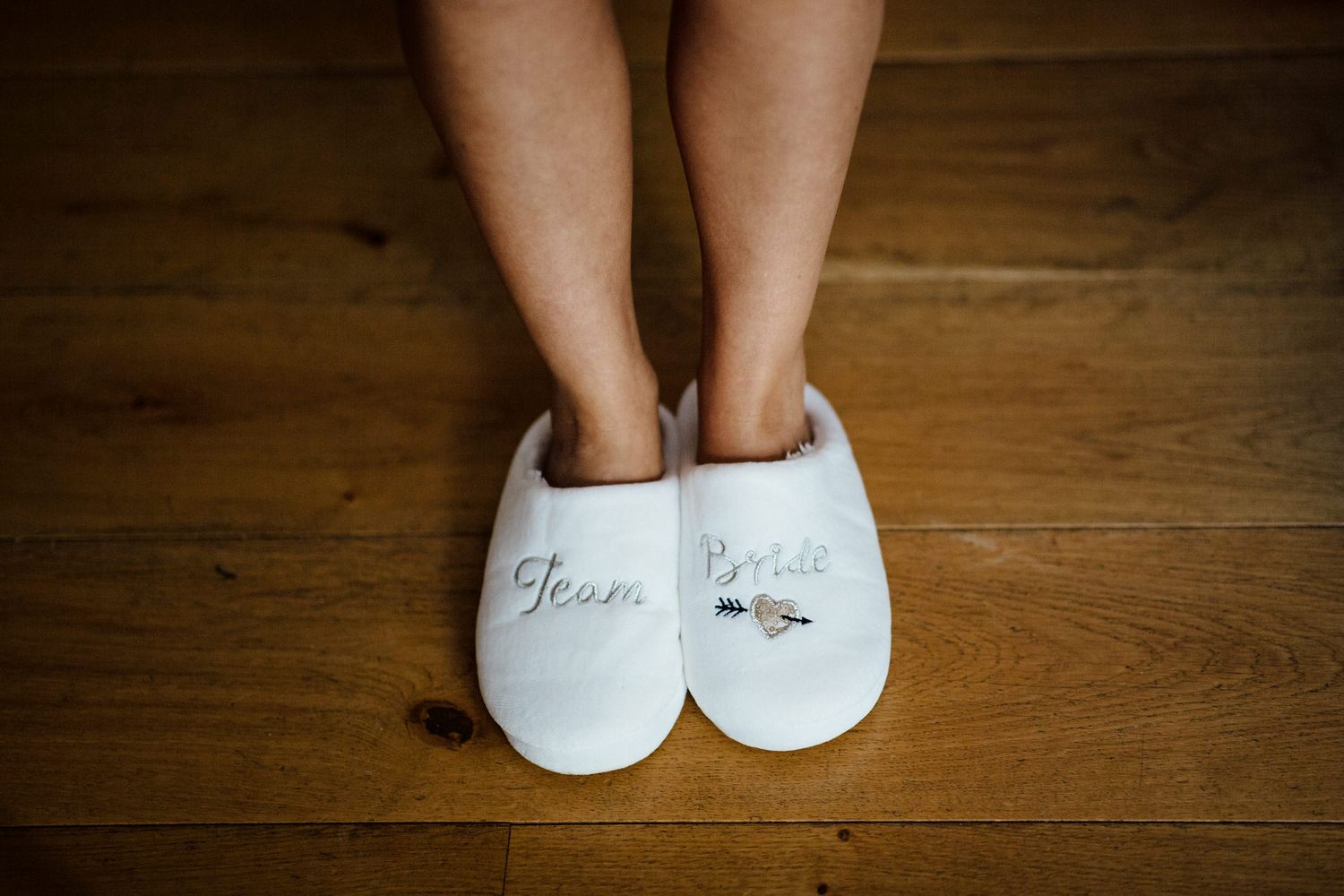 White slippers with 'Team Bride' text on wooden floor.