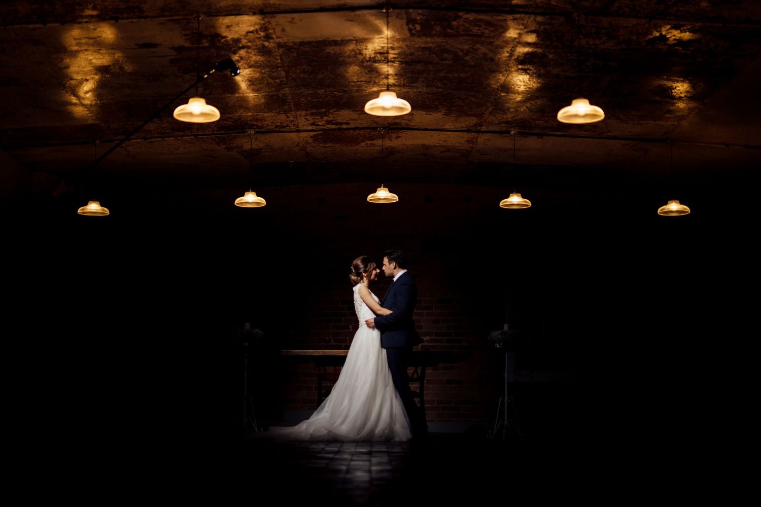 Dramatic lighting illuminates wedding couple dancing in an elegant venue.
