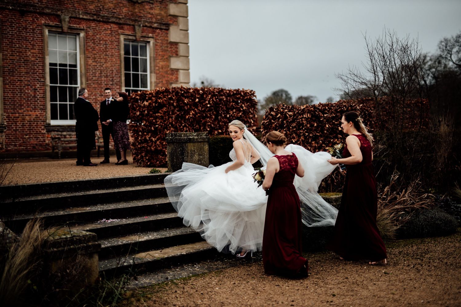 Wedding party ascending brick stairs outside a historic building on an overcast day.