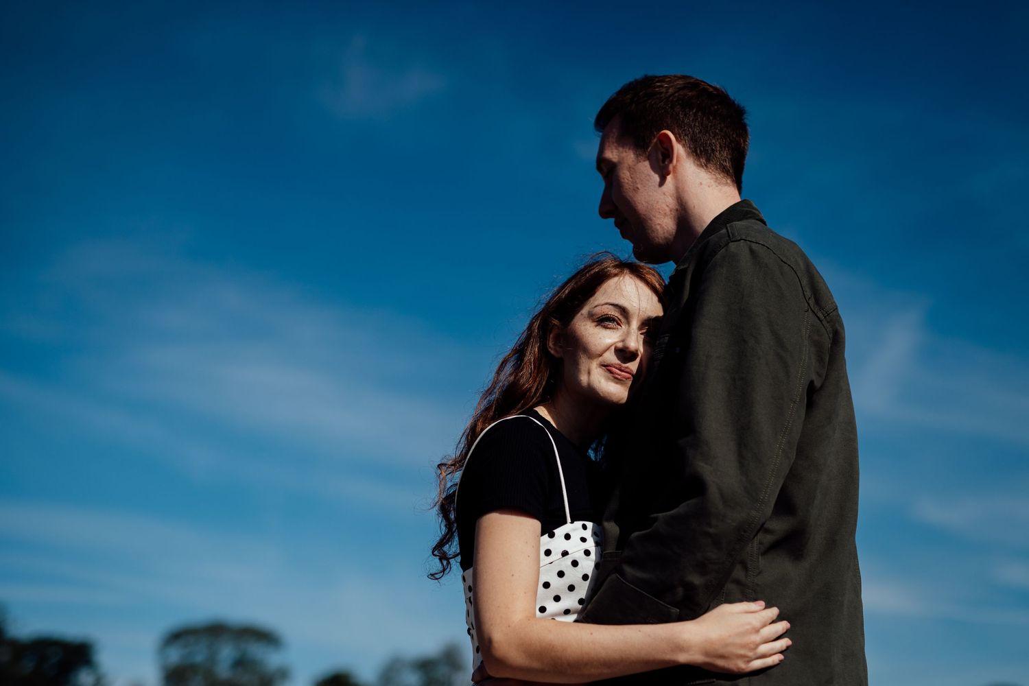 A romantic silhouette of a couple embracing against a vibrant blue sky background.