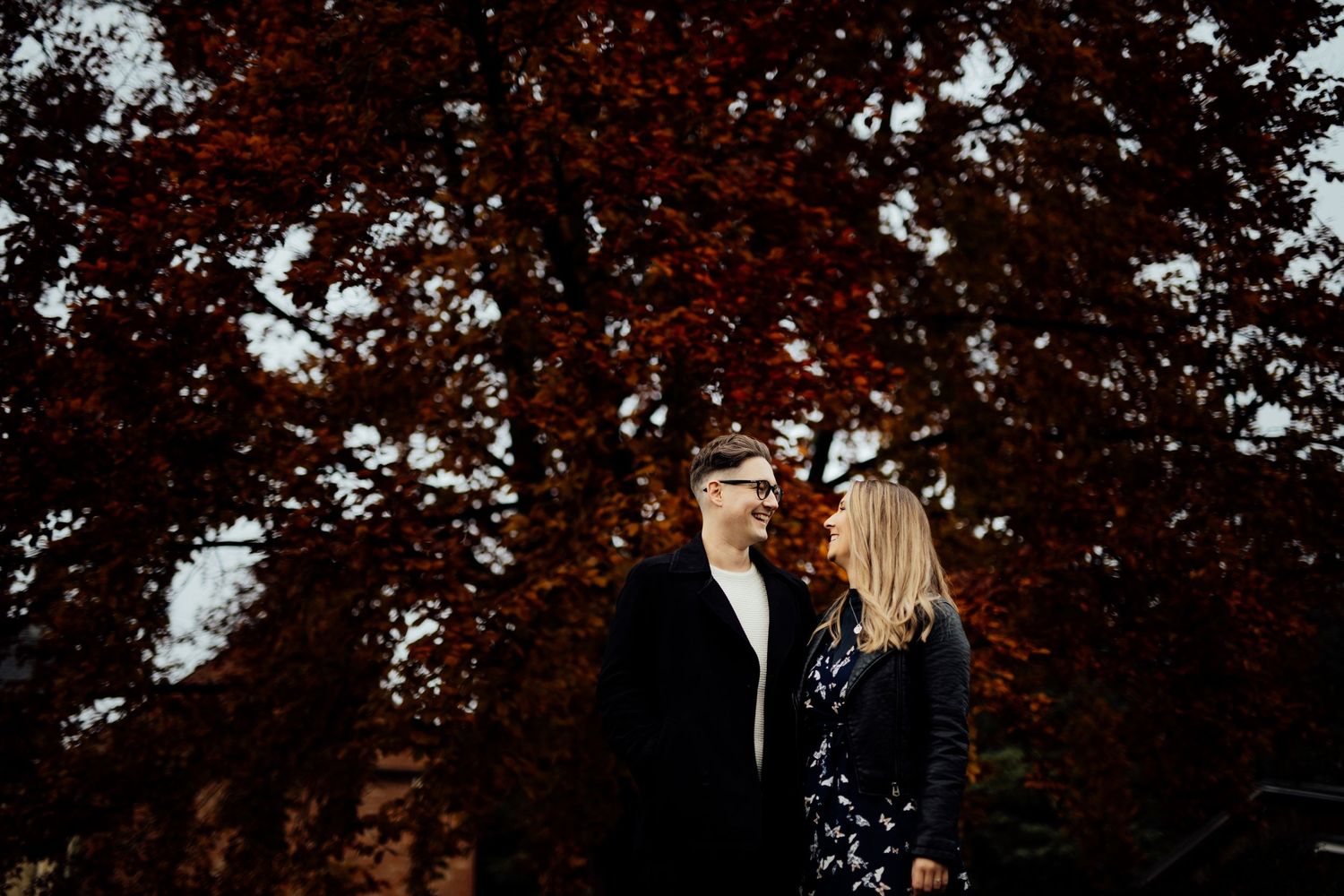 Red autumn leaves create natural canopy over couple's outdoor portrait.