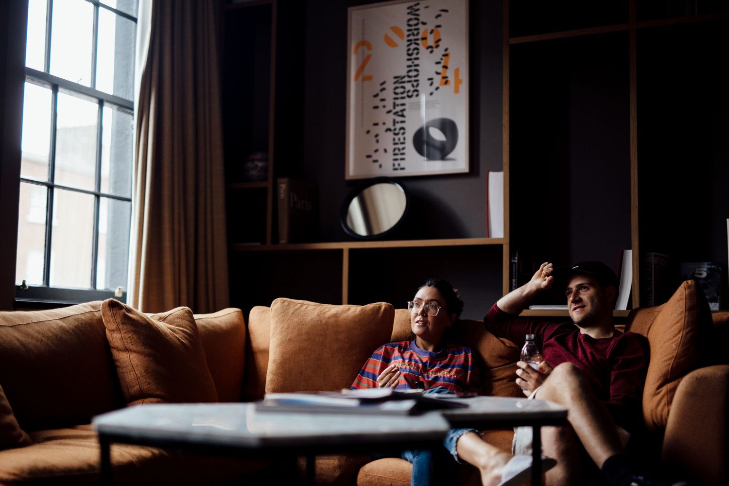 A cozy dark interior scene with natural window light and comfortable seating.