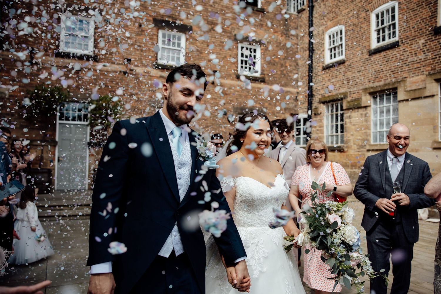 Wedding party celebration with confetti outside historic brick building.