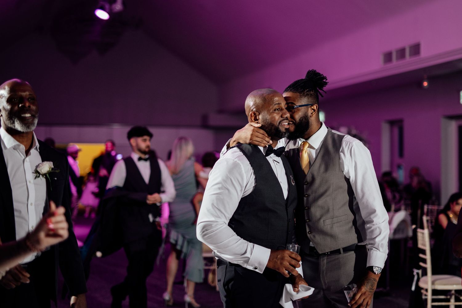 Wedding reception dance floor illuminated with purple lighting as guests celebrate.