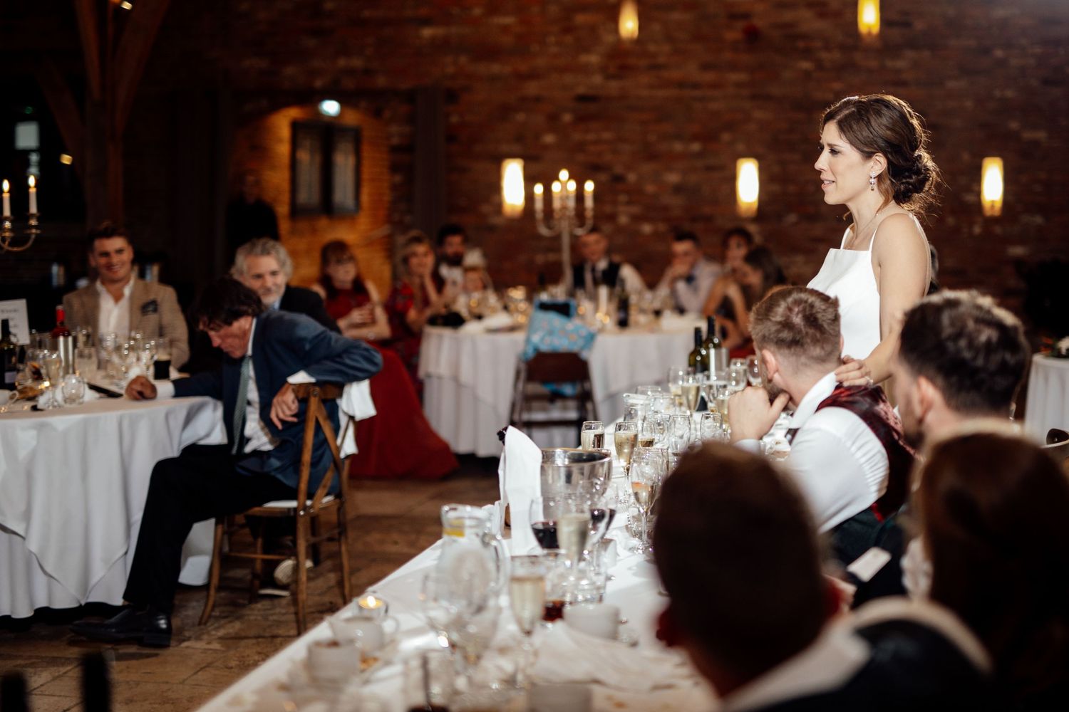 Wedding reception speech in a rustic venue with candlelit tables and exposed brick walls.
