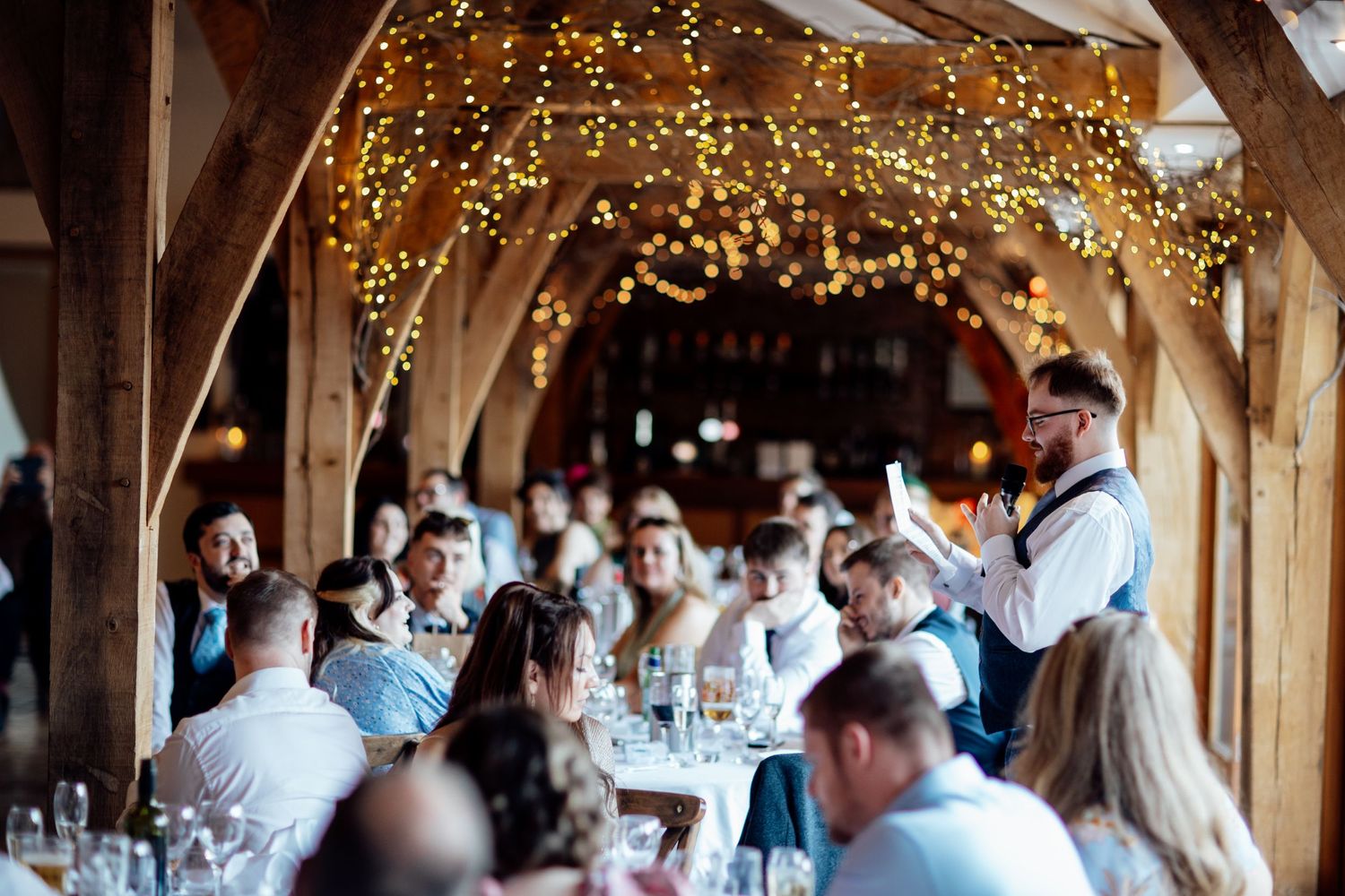Wedding reception venue decorated with twinkling fairy lights and wooden beam architecture.