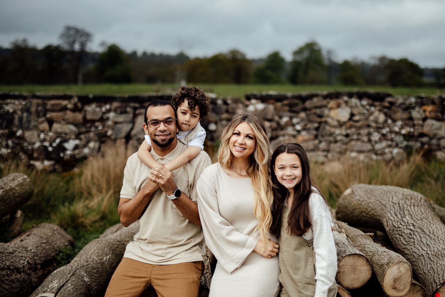 A family shares joyful moments while sitting on fallen logs during an outdoor photoshoot.