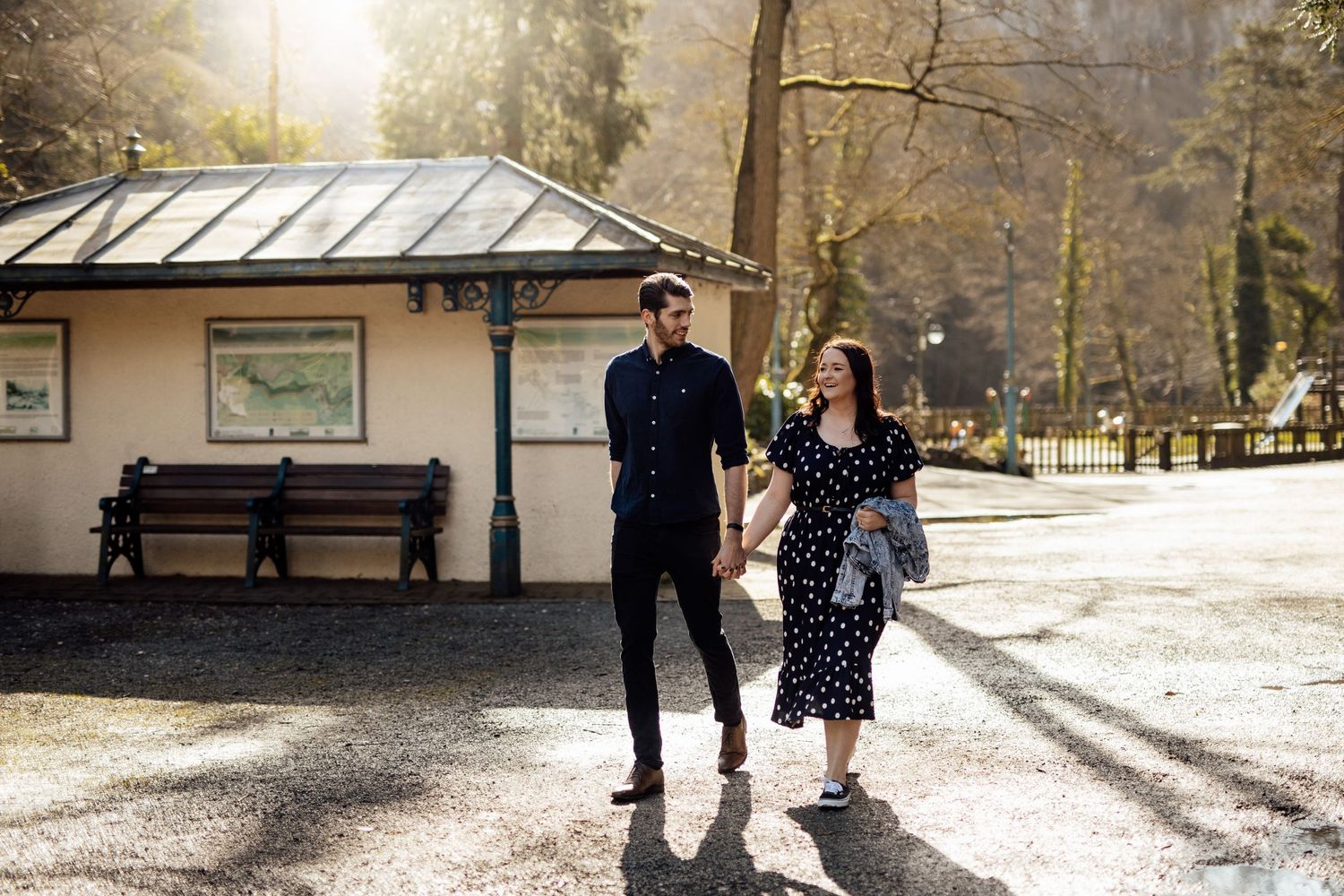 A couple stands in front of a vintage bus shelter during golden hour.