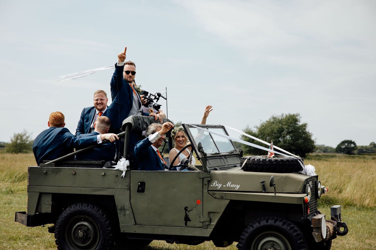 Wedding party riding in vintage military jeeps through countryside during outdoor celebration.