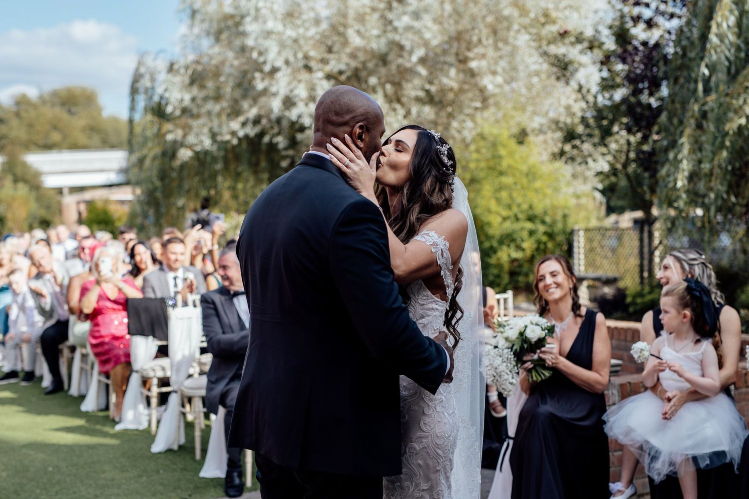Wedding guests gather outdoors for celebration on sunny day.
