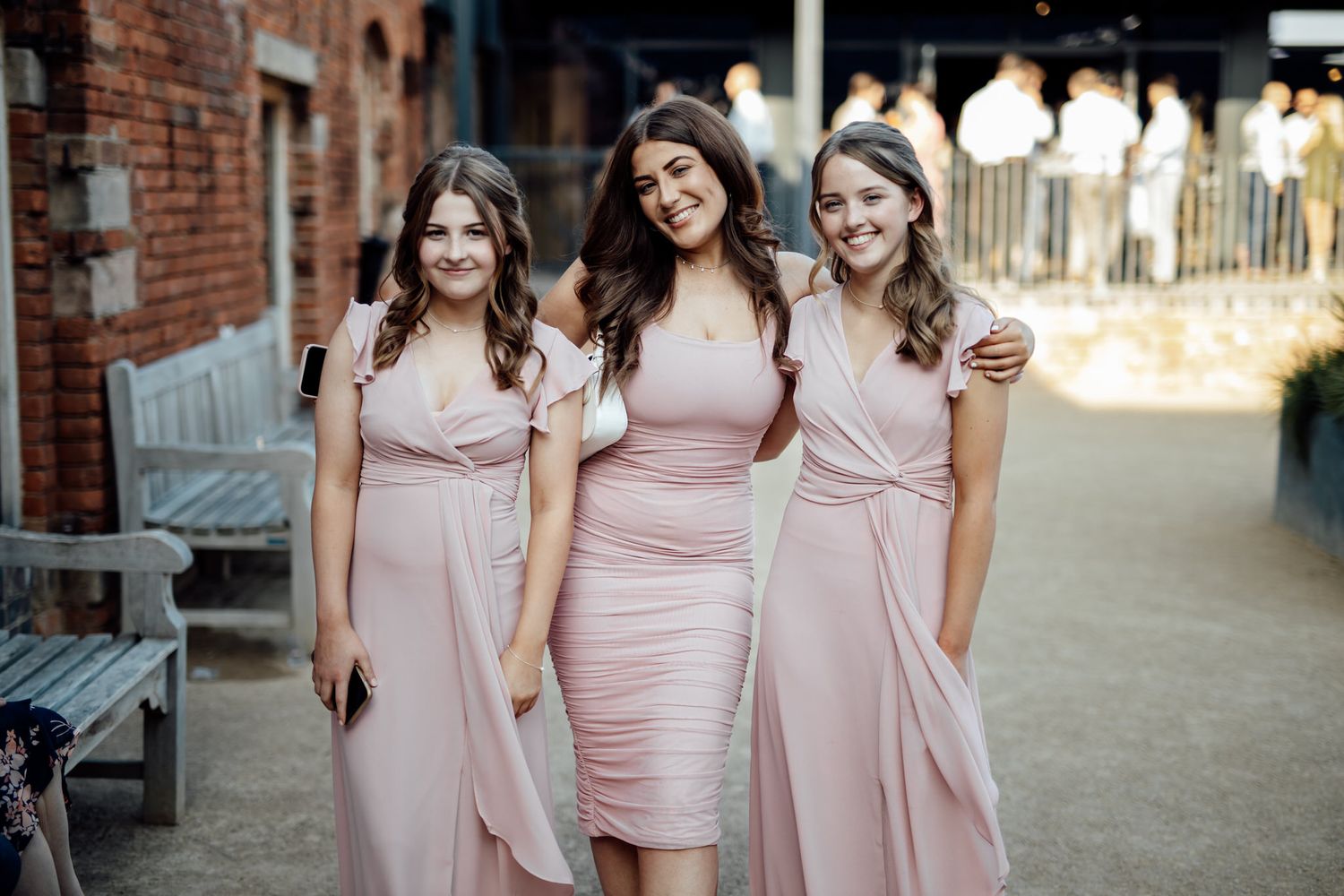 Bridesmaids in blush pink dresses walking together outside a brick building.