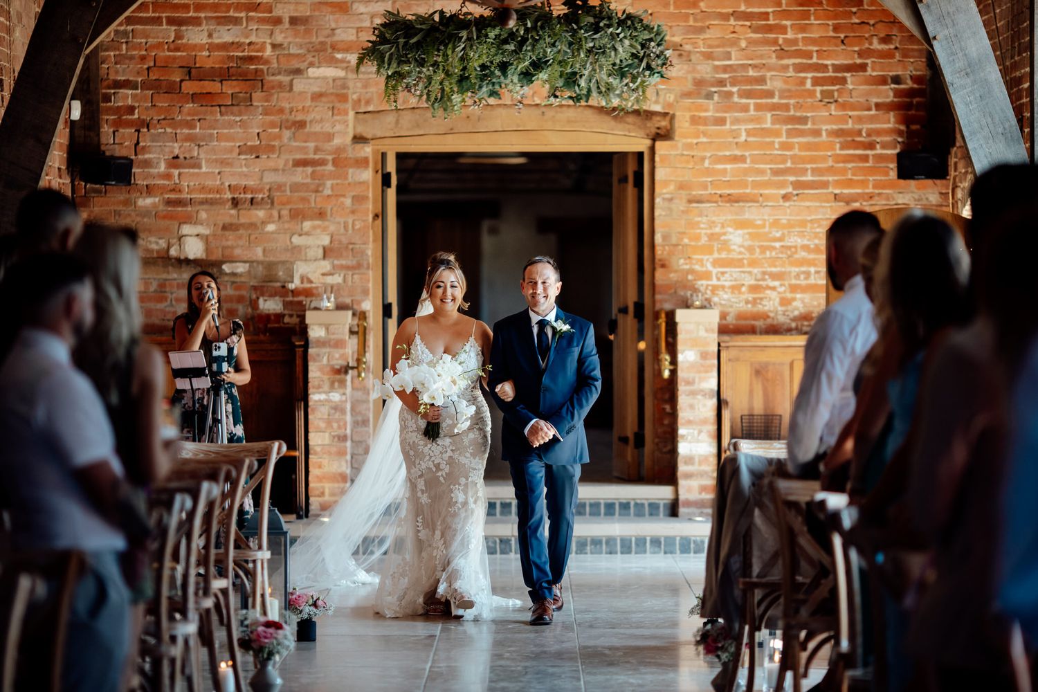 Wedding ceremony in a historic brick venue with greenery arch and guests seated.