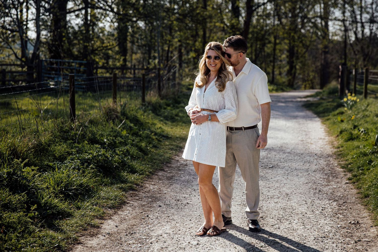 Couple walking hand in hand down winding gravel path through wooded area.