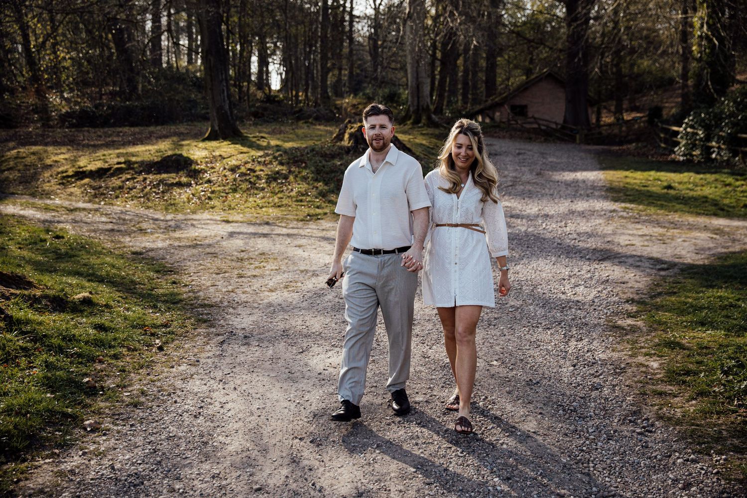 Two people walk together on a gravel path through green countryside.