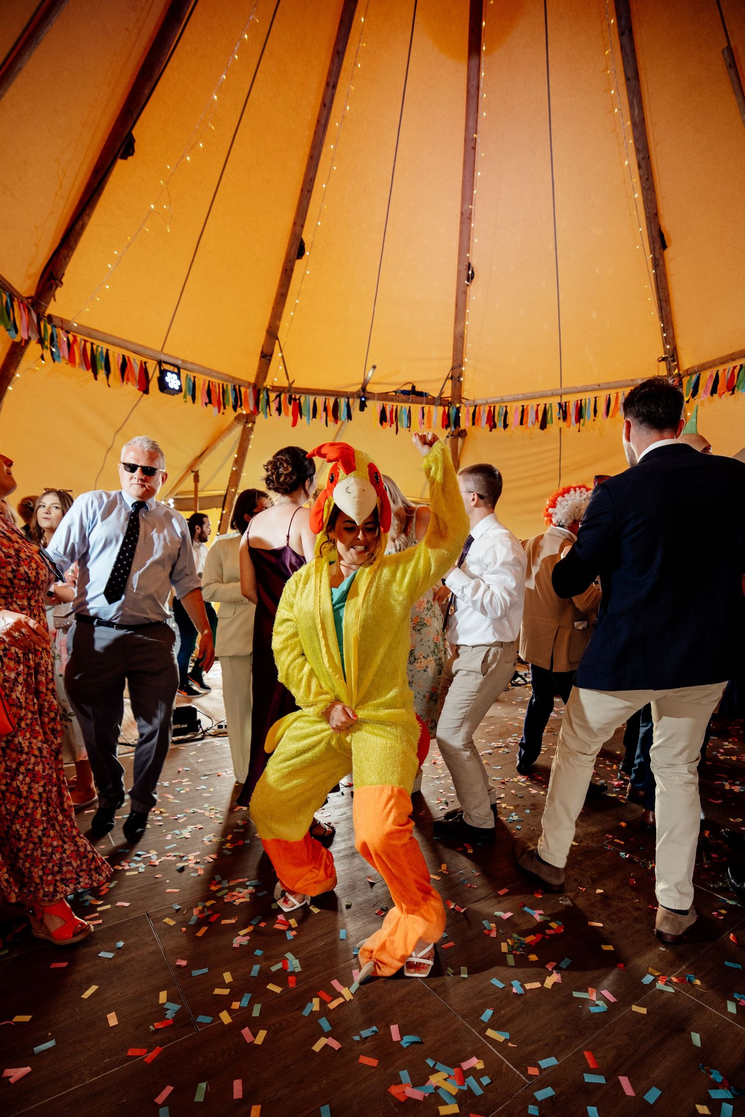 People dancing at a wedding reception inside a tipi tent with colorful bunting and confetti.