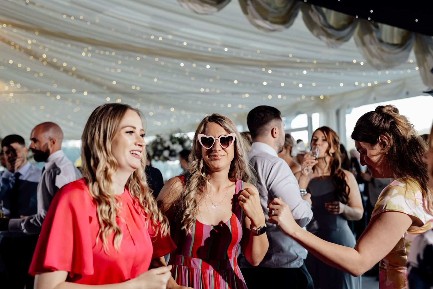 Wedding reception celebration under a tent with string lights and festive atmosphere.