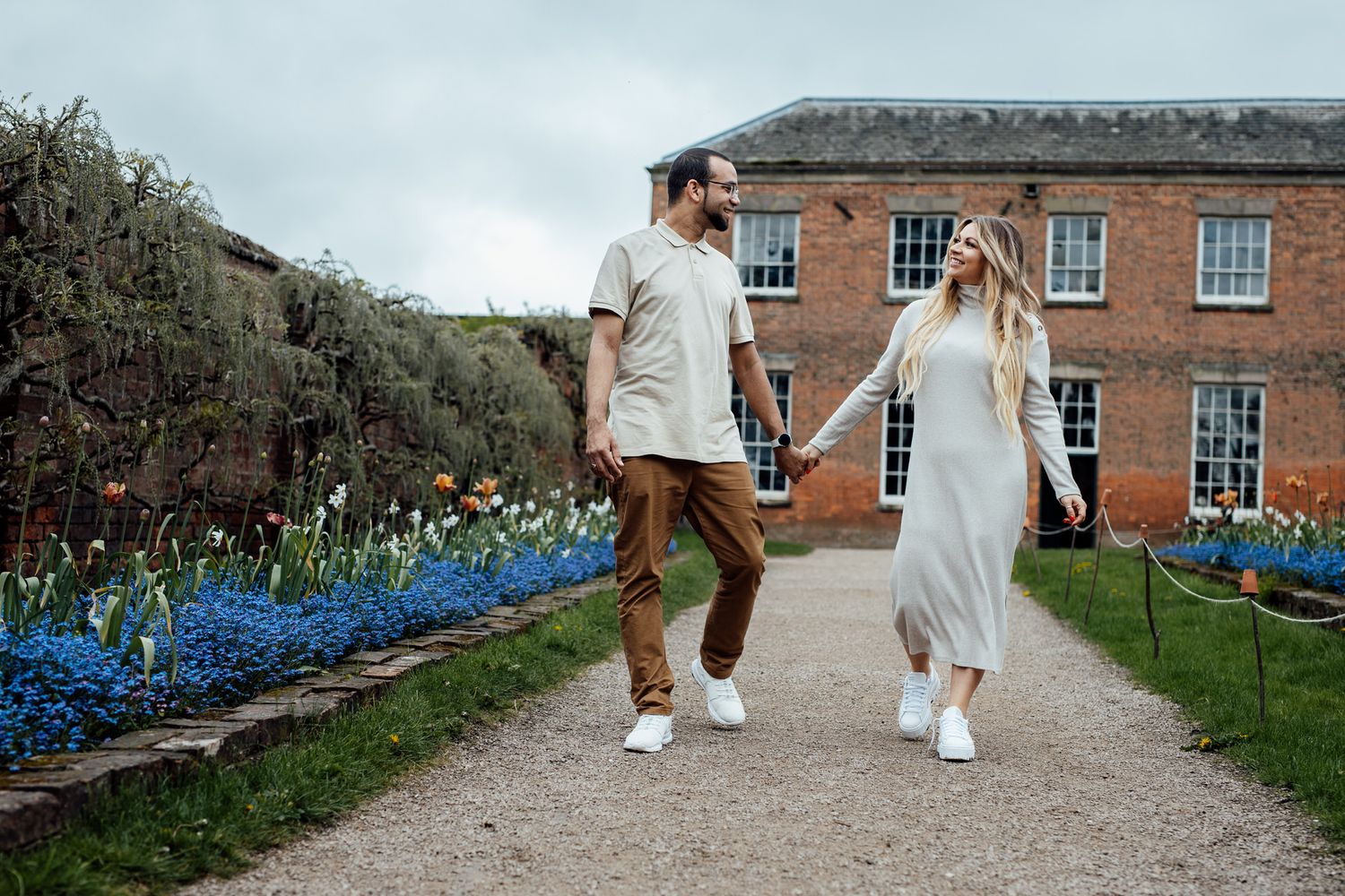 Family walking along a gravel path beside a red brick building and blooming flowers.