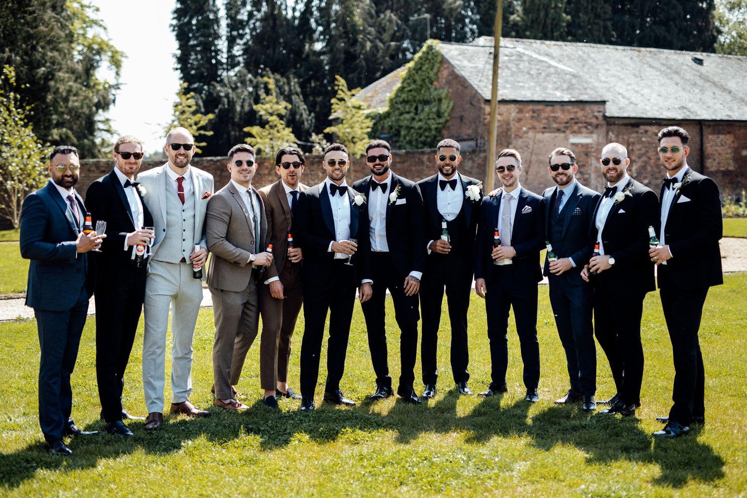 Large wedding party in formal attire poses on sunny lawn.