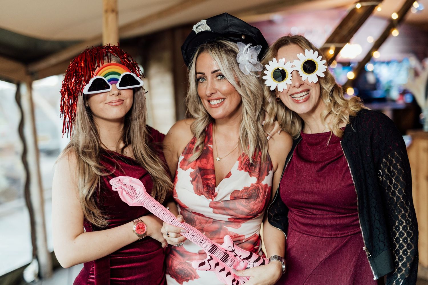 Three wedding guests wearing festive attire and novelty sunglasses pose together at celebration.