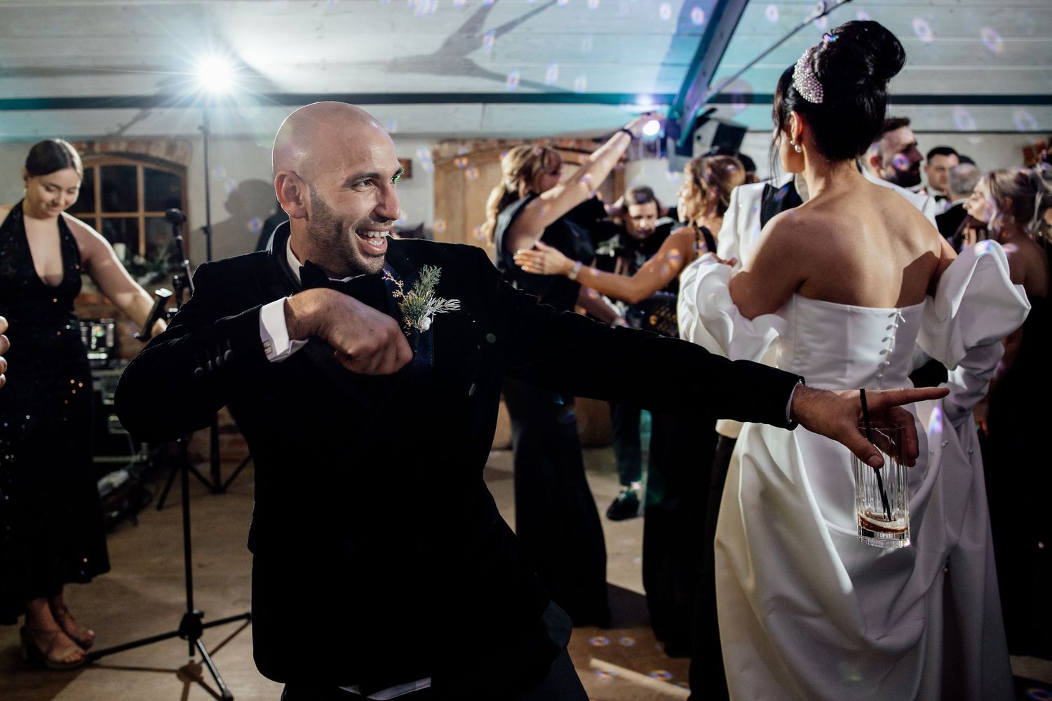 Wedding party members dance in pairs during an evening reception with dramatic lighting.