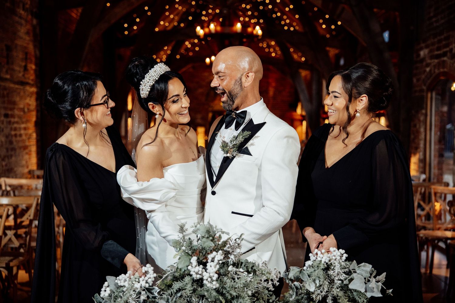 Wedding party gathers for group photos with matching bouquets against brick wall.