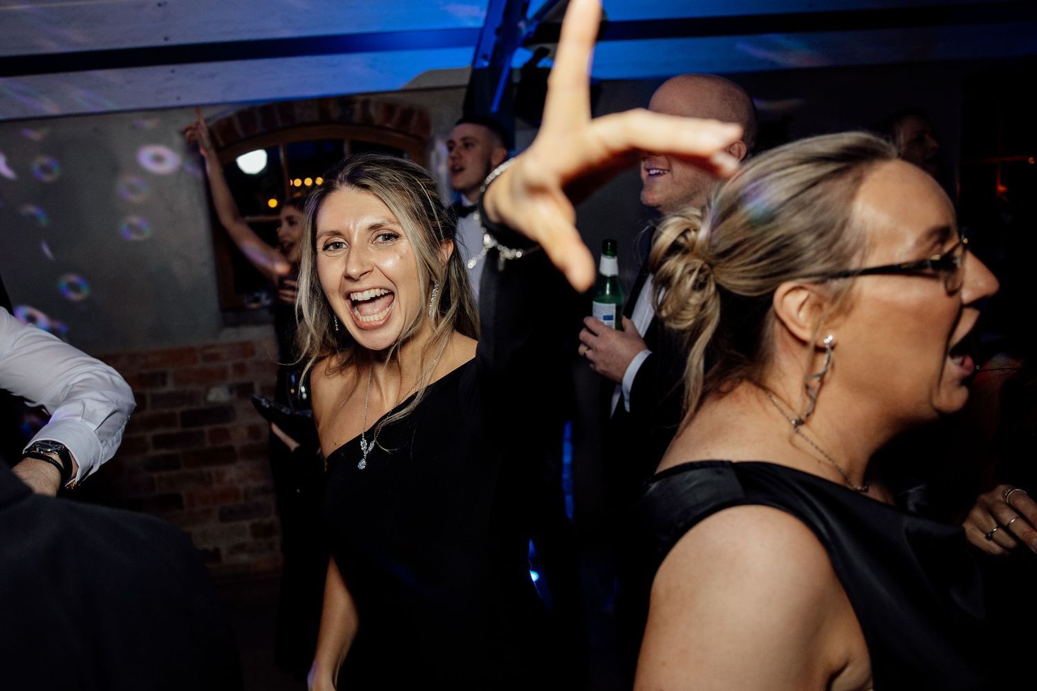 Wedding guests dancing and enjoying themselves under blue mood lighting at reception.