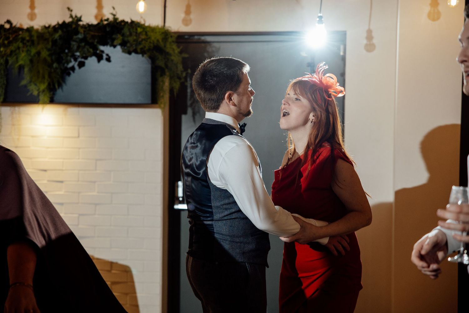 Couple dancing closely together at wedding reception, woman wearing red dress with floral hair accessory.