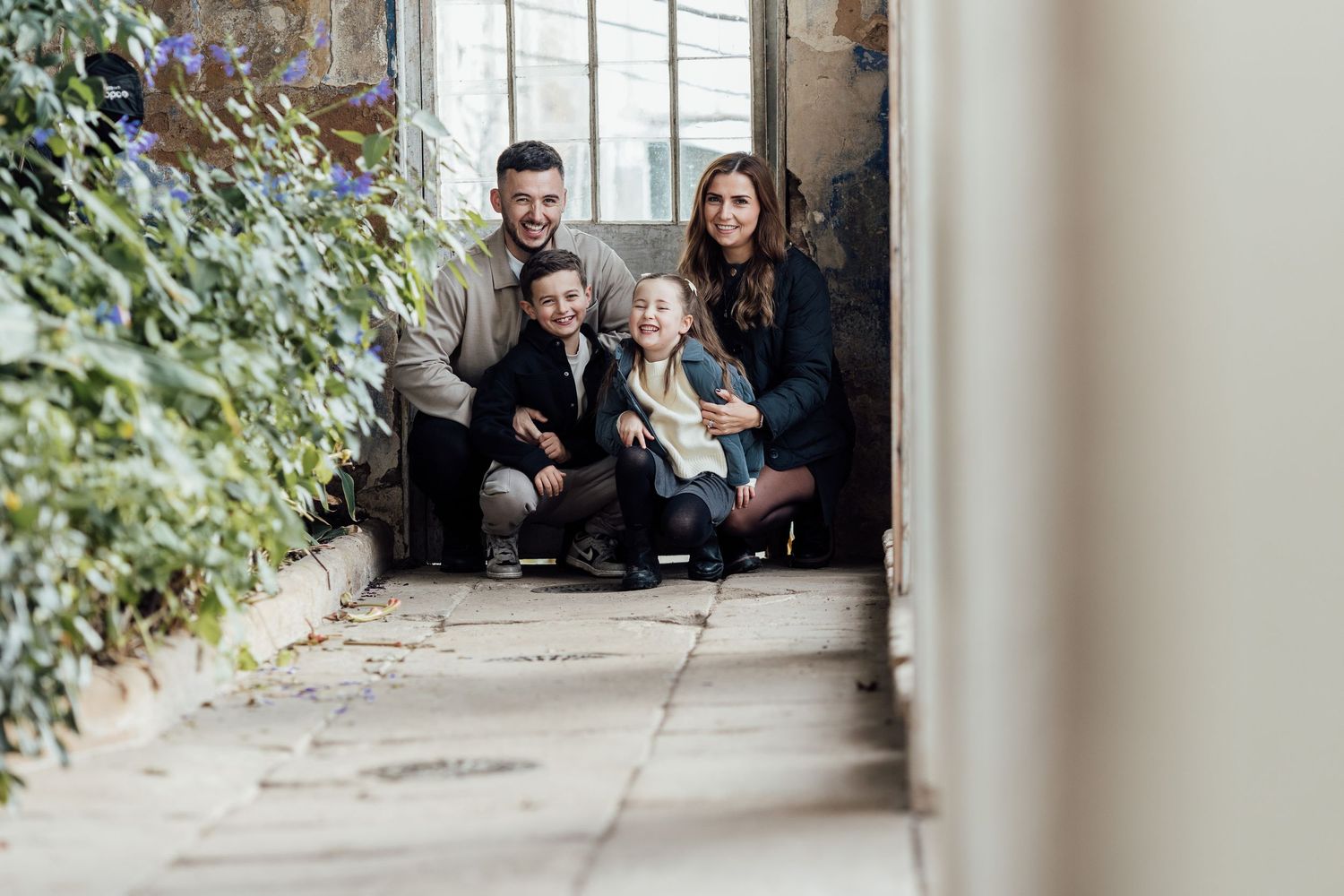 A family sits together on the floor in a bright, modern hallway with large windows.