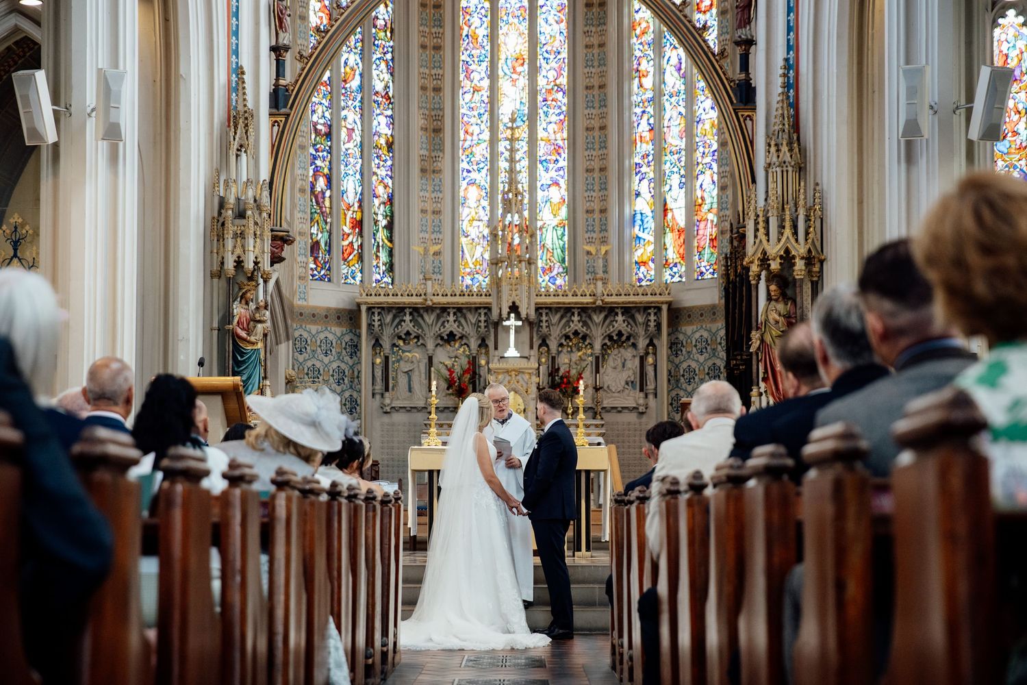 Traditional church ceremony with stained glass windows and gothic architecture in background.