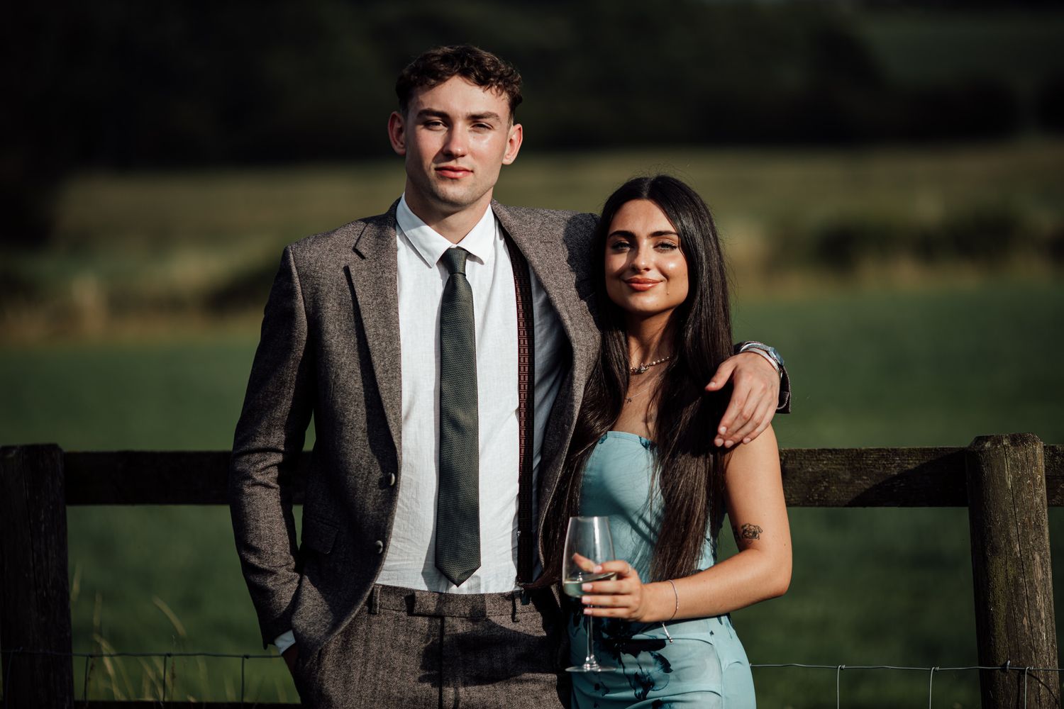 Couple poses against rustic wooden fence during sunset golden hour photo session.