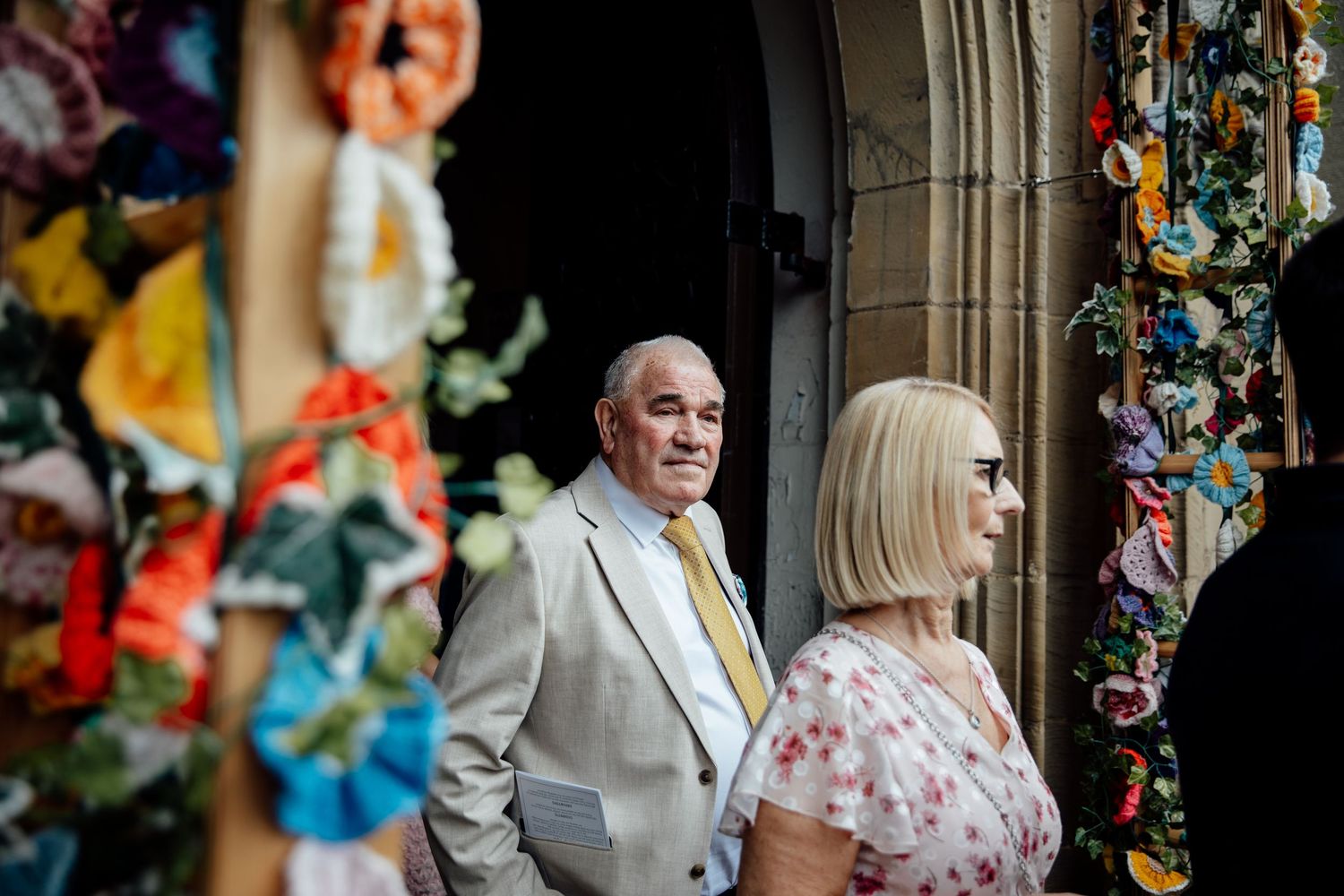 Wedding guests in formal attire gather near colorful floral decorations.