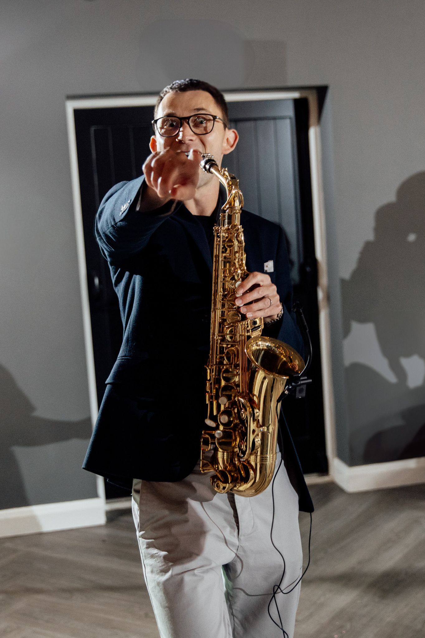 Musician plays saxophone in a minimalist room with dramatic shadows on the wall.