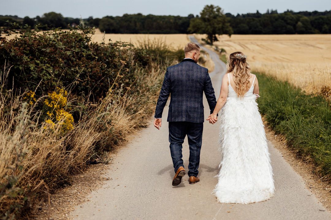 Couple walking hand in hand down a rural path surrounded by wheat fields.