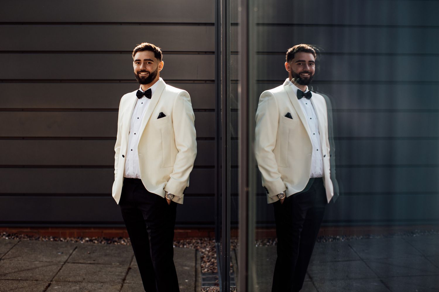 Groom in white tuxedo jacket poses against modern industrial backdrop.