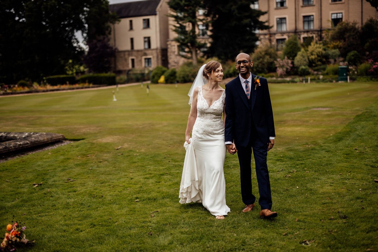 Bride and groom stand together on manicured lawn with historic building in background.