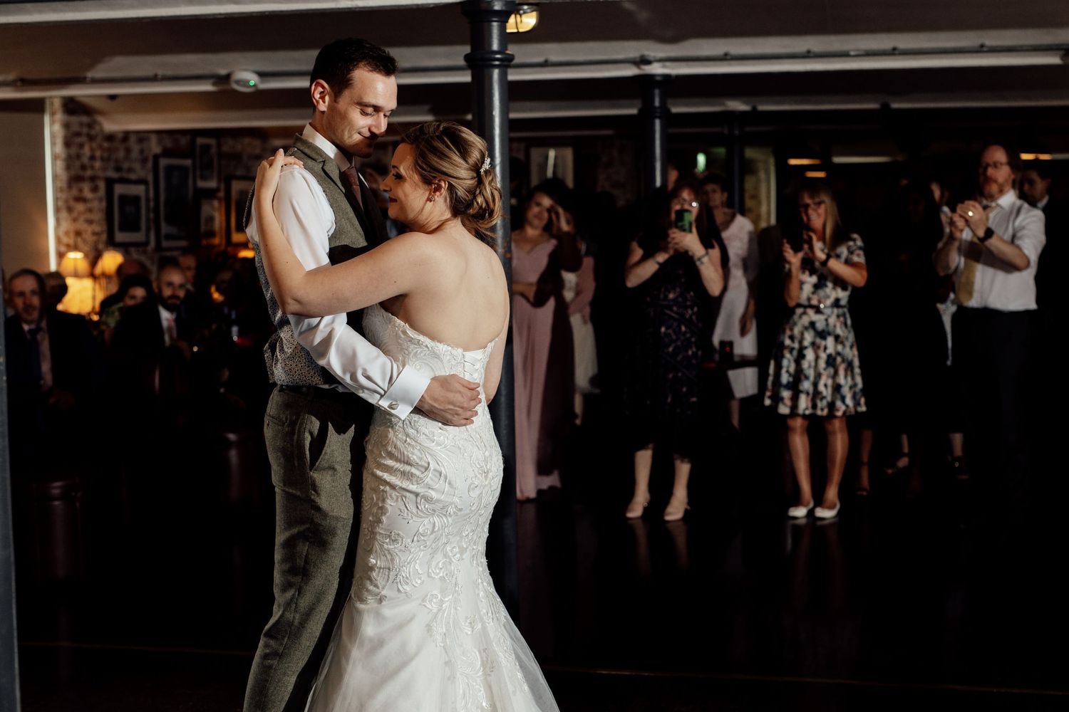 Couple shares their first dance at wedding reception while guests watch from the background.