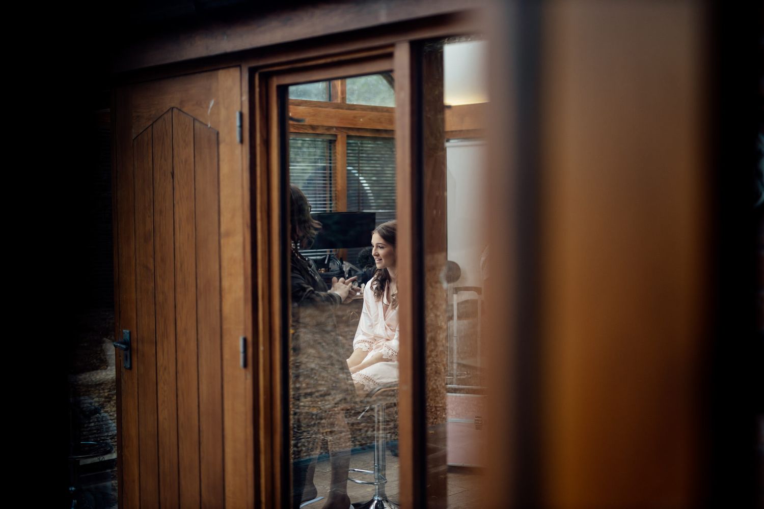 An artistic wedding photo framed through a doorway shows a glimpse of the bride.
