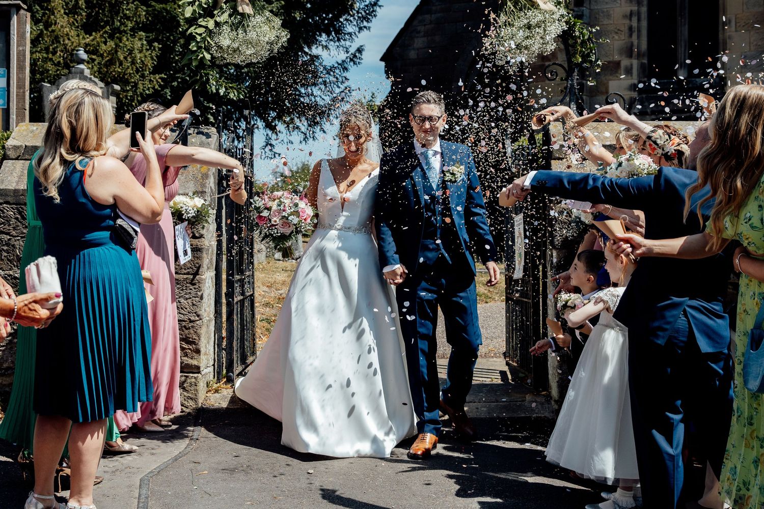 Wedding guests throw confetti over the newlyweds during outdoor celebration.