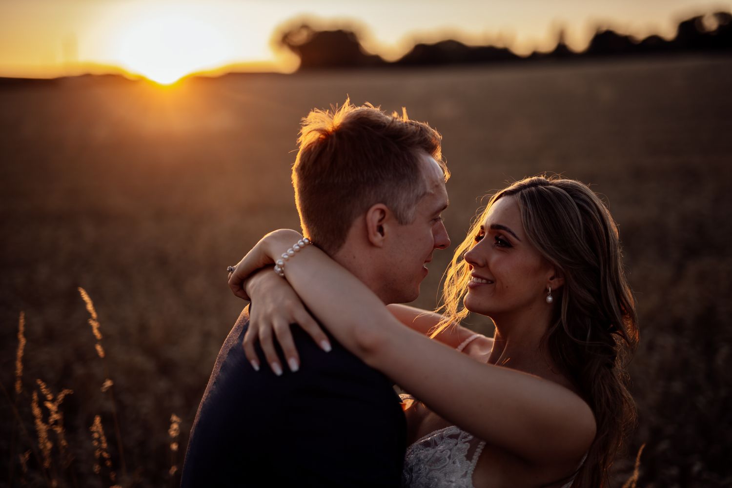 Newlyweds share an intimate moment in a sun-drenched field during golden hour.