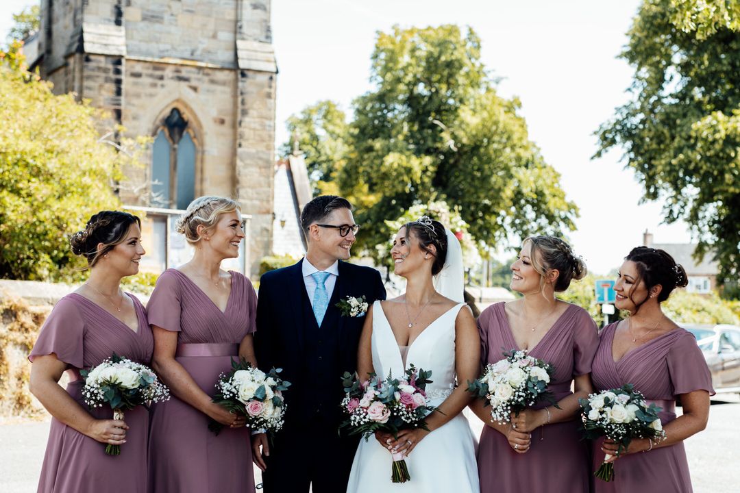 Wedding party posing outside a stone church with bridesmaids in purple dresses.