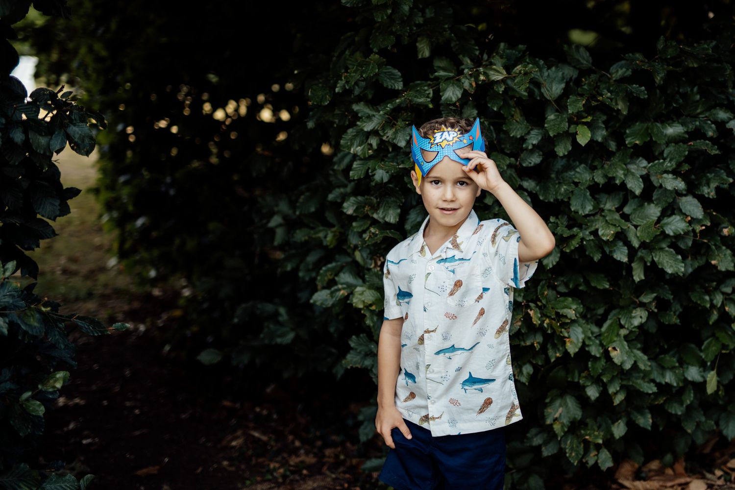 Young child in a patterned shirt playing in a garden setting.