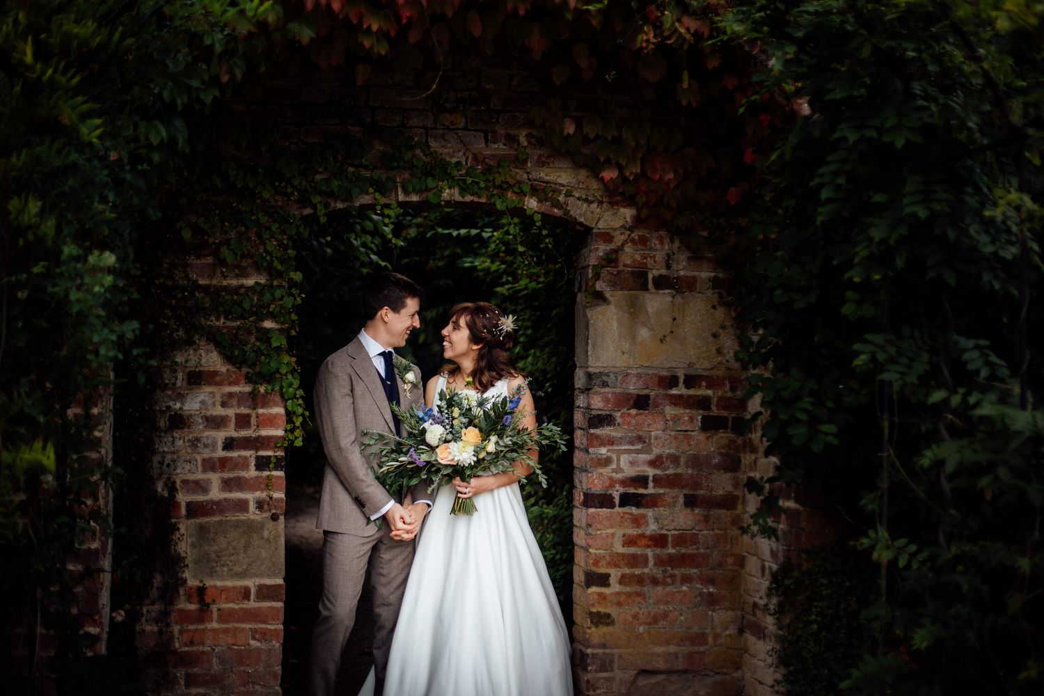 Romantic wedding portraits against a rustic brick wall with lush greenery.