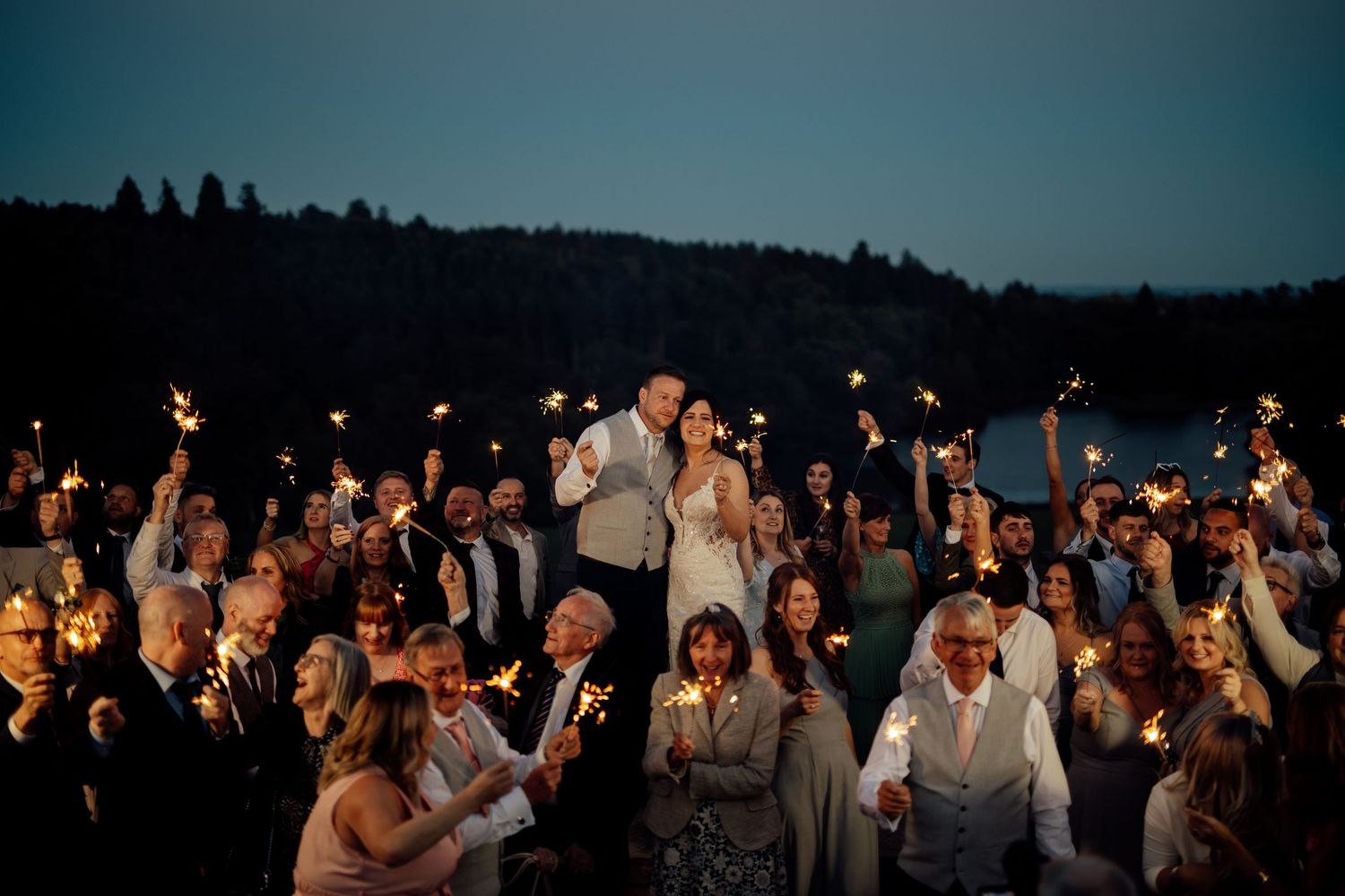 Wedding guests hold sparklers creating a magical nighttime celebration atmosphere.