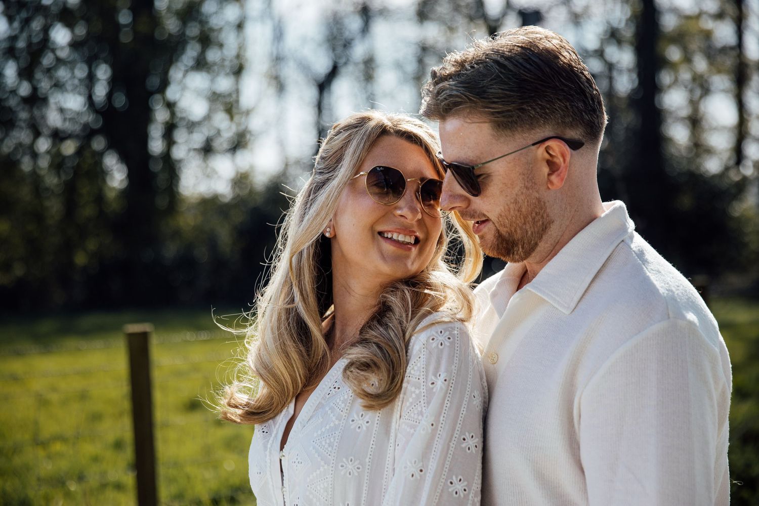 A romantic couple in white outfits share intimate moments in a sunny outdoor setting.