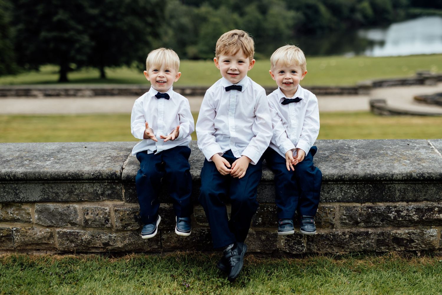 Three young children in matching outfits sit together on a stone wall outdoors.