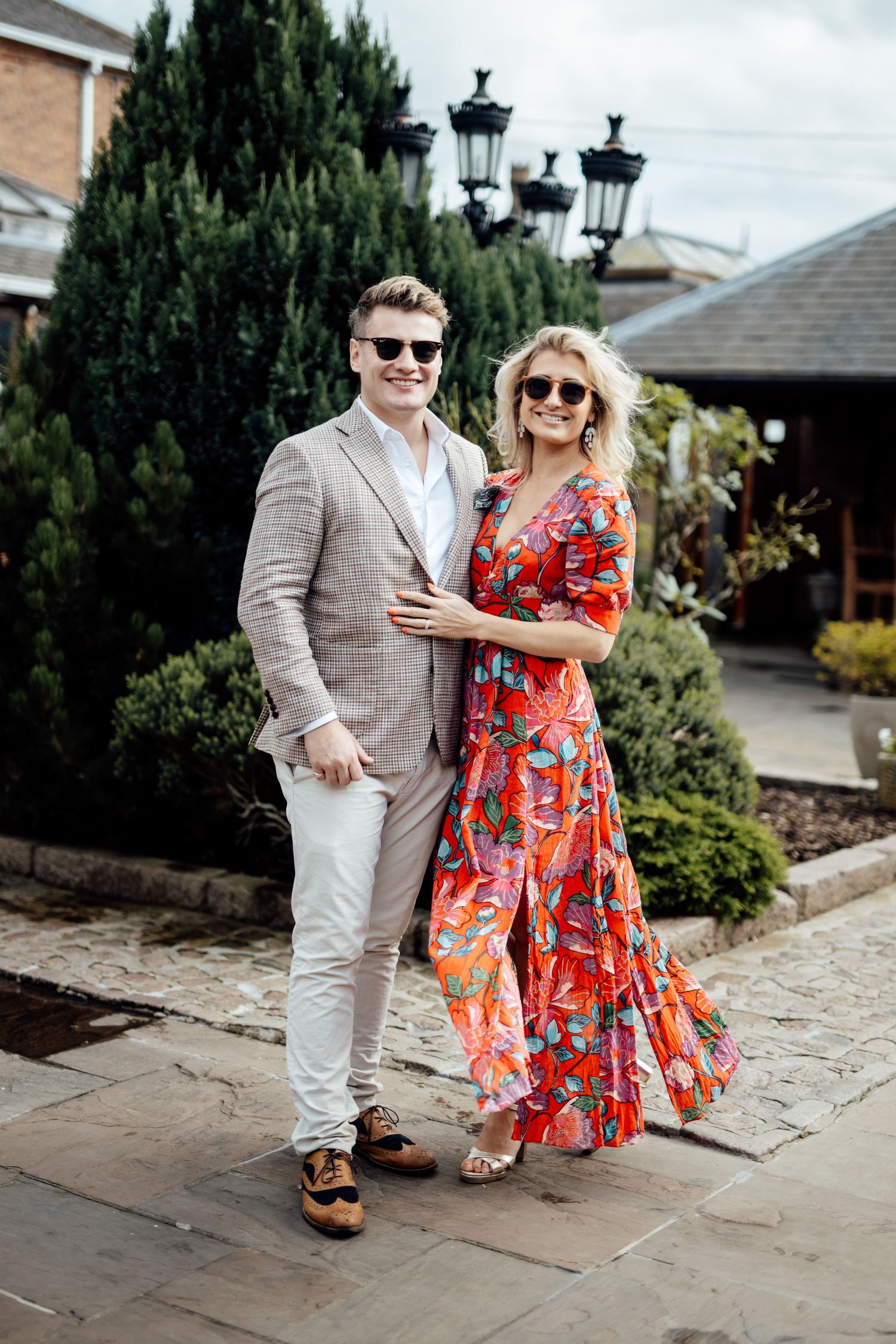 Couple in summer attire posing on stone pathway near garden.