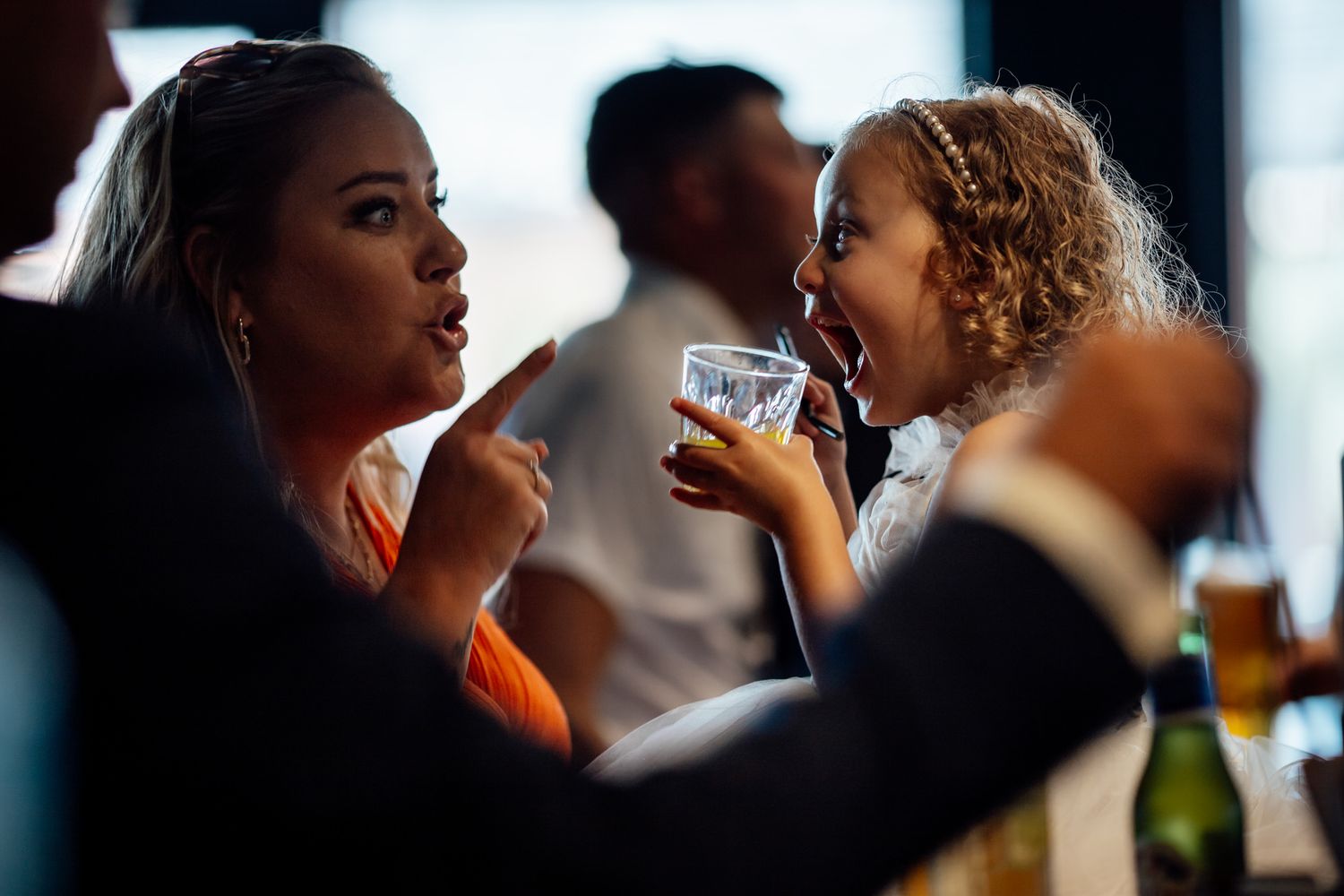 Silhouettes of wedding guests drinking and socializing at a dimly lit reception.