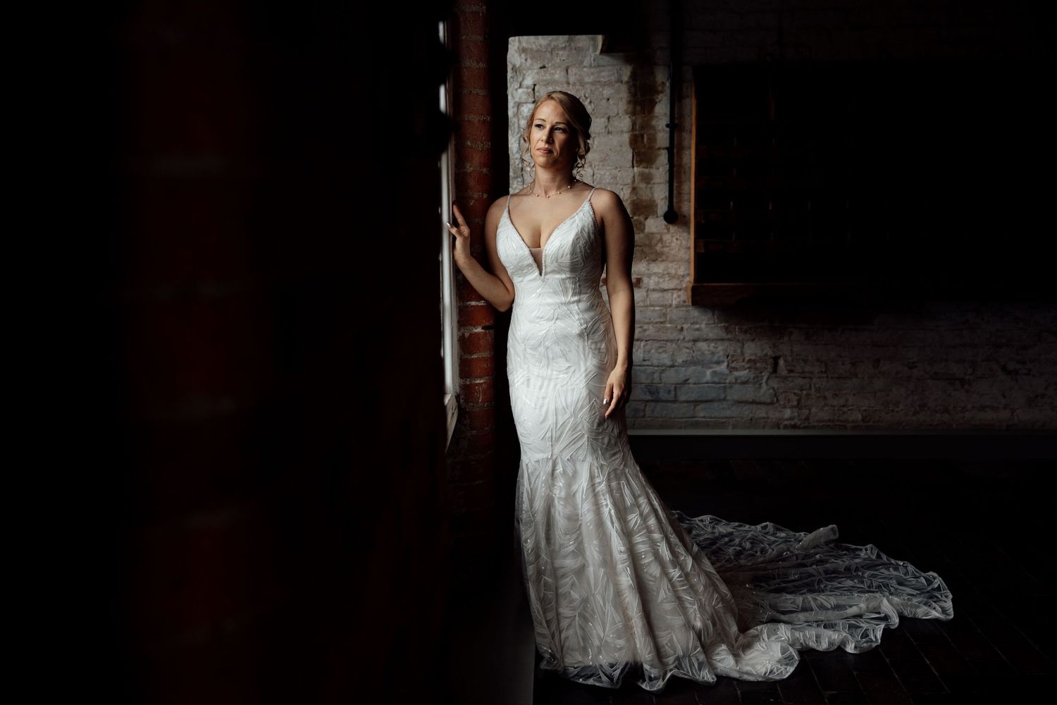 Dramatic lighting illuminates a white lace wedding dress in a dark indoor setting.