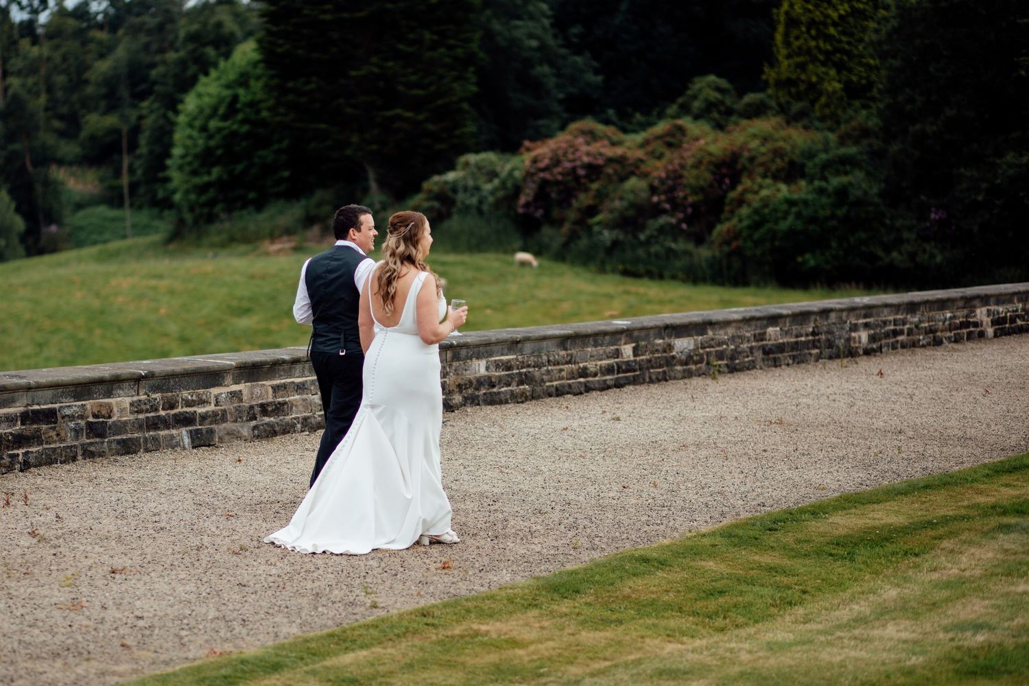Newlyweds walking along a stone path surrounded by green landscape.