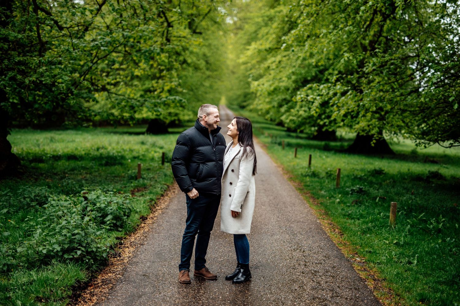 A couple walks along a tree-lined path during a romantic outdoor photo session.